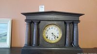 Front view of antique wooden mantle clock with four columns and round clock face with gold trim.