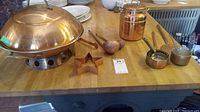 Copper kitchenware set displayed on a wooden table including a large chafing dish, star mold, ladles, and saucepans