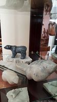 Photo showing three Inuit animal sculptures including black stone polar bear on natural stone base and two smaller light-colored animal sculptures.