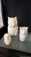 Front view of three carved owl sculptures in light stone material