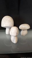 Three white stone mushroom sculptures grouped on a flat surface against a dark background.