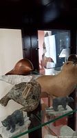 Photo showing all three sculptures displayed on glass shelving: wooden beaver on soapstone base, green stone walrus sculpture with ivory tusks, and gray seal skin style sculpture.