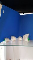 Photo showing all four small marble bear sculptures arranged in a row on a glass shelf against a blue backdrop.