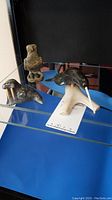 Set of three inuit soapstone sculptures displayed on glass shelf: bird on stand, walrus, and abstract human figure.