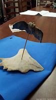 Sculpture of a soapstone bird mounted on a natural antler base displayed on a table with blue cloth underneath.