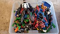 Top view of plastic bin filled with assorted superhero action figures including Venom and Spider-Man prominently visible on top