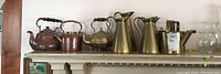 Wide view showing all brass and copper items on mantel: copper picnic kettle, brass teapots, jugs, and watering cans.