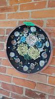 Hand painted wooden dish with floral design mounted on brick wall, 15 inches diameter.