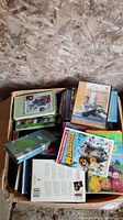 Box of assorted DVDs and VHS tapes with kids movies such as Madagascar, Teletubbies, Core Challenge exercise DVDs and more.