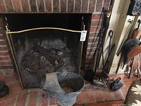 Full view of fireplace hearth with brass fireplace screen, ash can, and fireplace tools including shovel, brush, poker, and sad iron on holder.