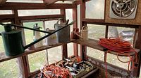 Photo of various garden watering cans, sprayers, orange extension cords, portable work lights and hand tools placed on wooden shelves in a garage.
