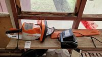 Trimmer, battery and charger laid out on wooden shelf under window
