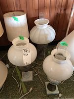 Group photo showing four lamps: one wood base lamp with fabric shade and three vintage milk glass shaded oil lamp style lamps with clear chimneys, all placed on floor.