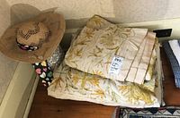 Photo showing piled embroidered linens with floral patterns and straw hat placed on top.