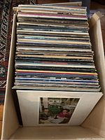 Cardboard box filled with vertically stacked vinyl LP records showing a variety of album covers.