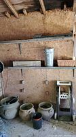Overall view showing three ceramic pots on floor and metal vintage hose reel on right under shelf with other pots and containers on it.