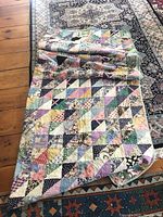 Full view of the folded quilt on a hardwood floor with another rug underneath, showing the overall patchwork pattern and size.