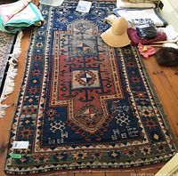 Full view of rectangular oriental rug on wooden floor showing central medallion, border pattern, fringed ends and overall wear.