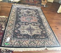 Rug laid flat on wooden floor showing full pattern and borders including fringe on one end.