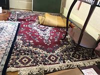 Full view of the red oriental rug with floral and geometric patterns, showing fringe and adjacent flooring and furniture