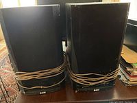 Photo showing a pair of black B&W speakers with wires wrapped around them and the B&W logo on front bottom.