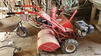 Front-side view of red Troy-Bilt tiller showing tines and handles