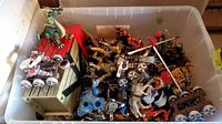 Photo of plastic toy figures and castle pieces inside a clear storage bin showing multiple medieval fantasy characters and accessories including horses, warriors, and dragons.