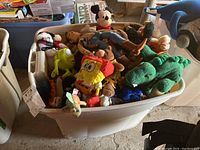 Bin filled with assorted character plush toys showing variety and condition.