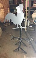 Front view of the weather vane showing rooster silhouette and base with compass directions.