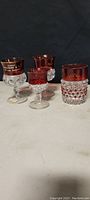 Front view of 4 Victorian ruby flash glasses on a neutral background. Includes marked souvenir and hobnail style designs.