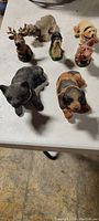 Seven animal bobbleheads arranged on a white surface including dogs, bear, pig, deer, and sheep.