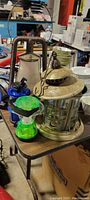 Antique-style metal lantern with glass panels next to modern green light lantern on a table with other items.