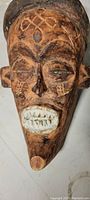 Front view of the wood carved face mask showing detailed facial features and painted white teeth.