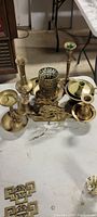 Photo showing various brass decorative items including candle holders, incense holder, napkin holder, and bell, arranged on a table.