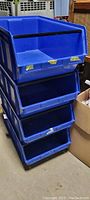 Four blue stackable plastic storage bins stacked vertically showing open front bins.