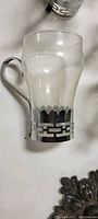 Close-up photo of one vintage clear glass cup with silver holder showing handle and decorative cut-out design.
