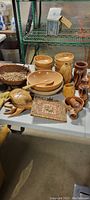 Photo of assorted wood kitchen items on a table including bowls, spoons, cups, pepper grinder, and woven mat