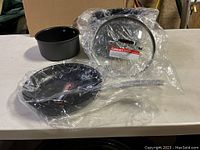 Three-piece set of Cuisinart non-stick cookware consisting of two pots and one frying pan with lid, all new in plastic packaging.