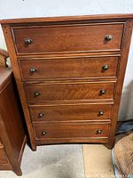 Front view of the mahogany colored chest of drawers, showing five drawers with metal knob handles.