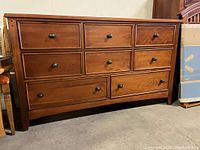 Front view of mahogany colored wooden dresser with nine drawers and metal knobs.