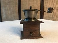 Photo of the antique coffee grinder showing wooden base, small drawer, and metal grinding bowl with crank handle.