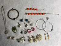 Overview of assorted jewelry on gray background including bracelets, earrings and pins