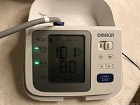 Front view of Omron blood pressure monitor display showing systolic, diastolic, and pulse readings with buttons visible.