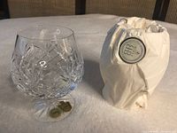 Pair of clear lead crystal brandy snifter glasses with one glass wrapped in white tissue paper showing Belfour logo