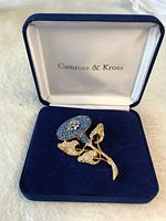 Gold-tone flower brooch with blue and clear rhinestones in original blue velvet box with white satin lining and Camrose & Kross branding.