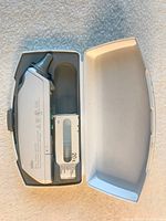 Digital infrared thermometer shown inside a white plastic carrying case with one nozzle cover visible.