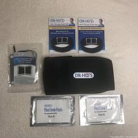 Items laid out: Dr. Ho's branded back belt, two instruction manuals in English and French, packaged TENS replacement pads labeled FlexTone Size B, a small device in plastic package with wire (likely TENS control unit).