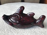 Fish-shaped carved container in dark reddish-brown with black accent carvings, showing side view