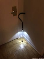 Walking cane standing upright, LED lights at the base illuminating floor and wall, showing light functionality and height.