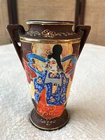 Photo of front side of mini vase showing hand painted Japanese figure in traditional costume with vibrant blues, reds, and gold accents